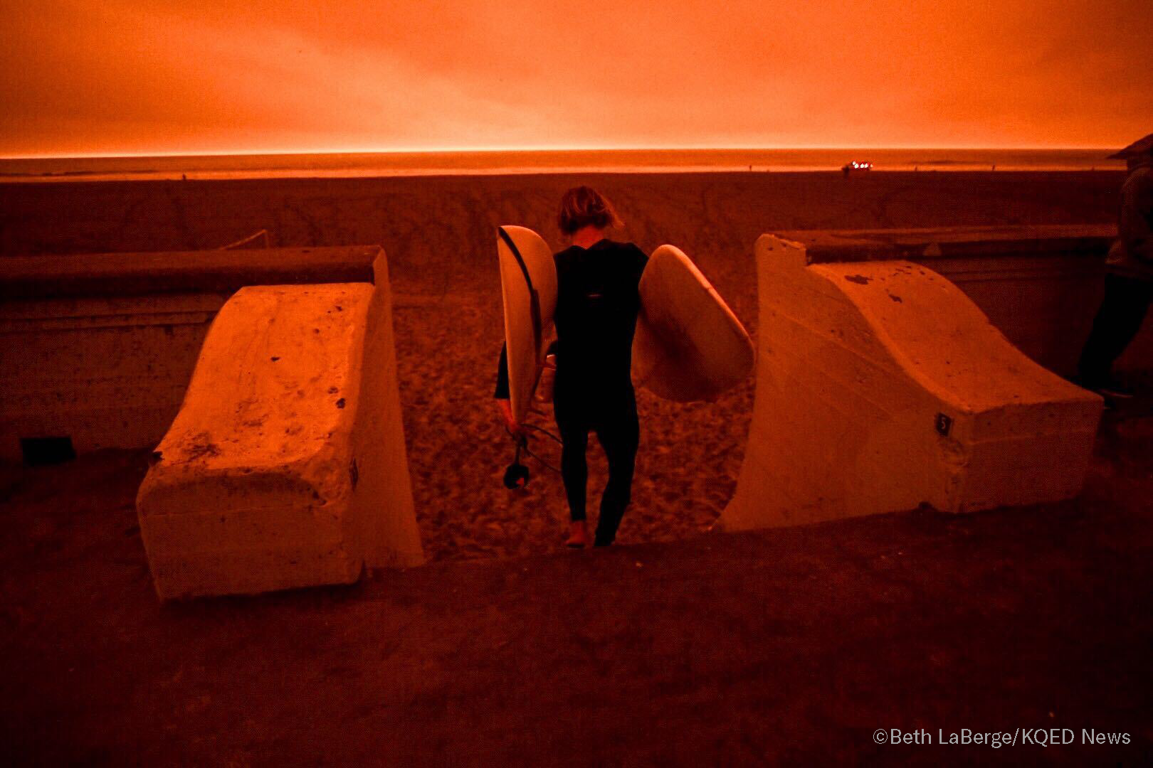 A surfer heads to Ocean Beach in San Francisco under smoke-filled orange skies, on Sept. 9, 2020.