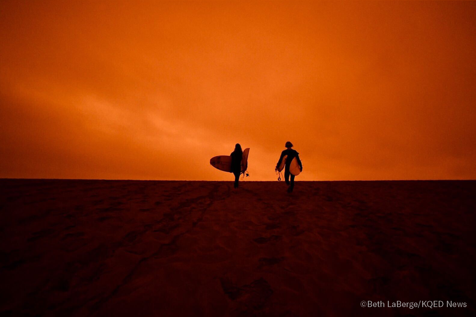 Surfers head for the the waves of Ocean Beach in San Francisco under smoke-filled orange skies, on Sept. 9, 2020.